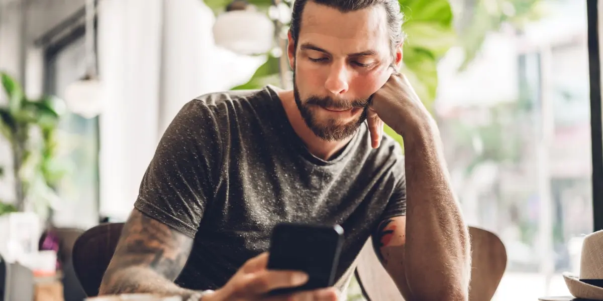 A person sitting in a cafe, scrolling on their smartphone, researching the average social media specialist salary