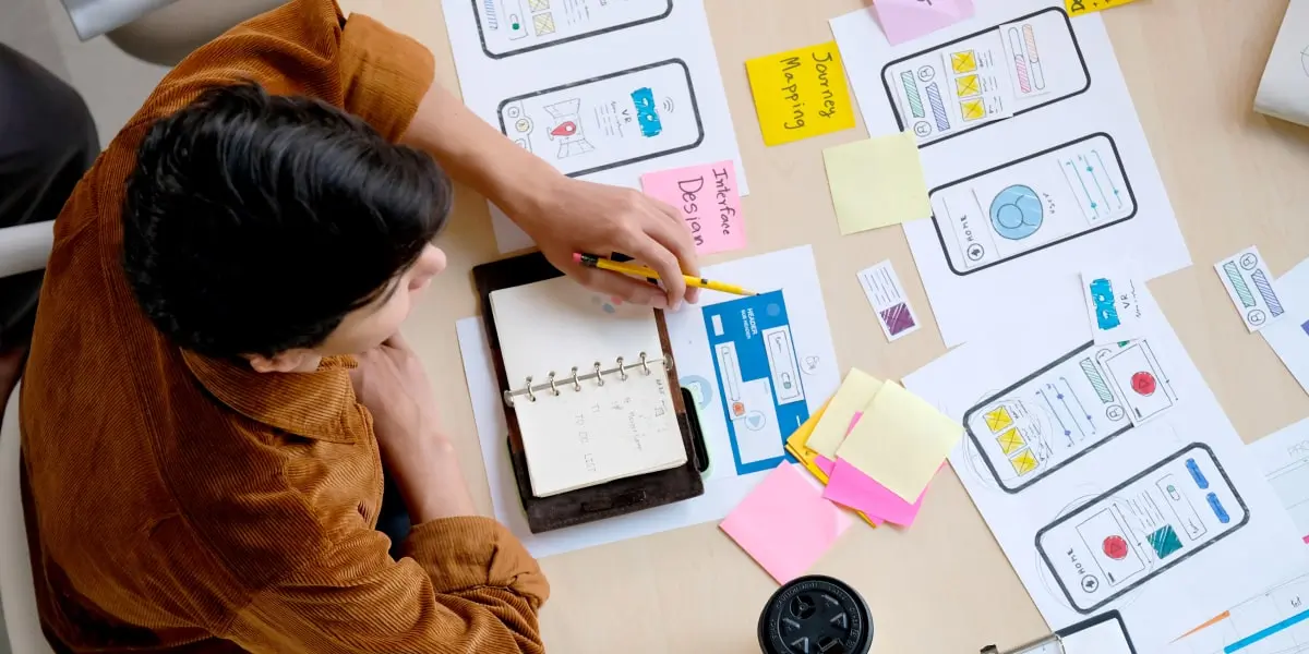 A man doing a free UX design course sits at a table with journey mapping app screens printed out in front of him.