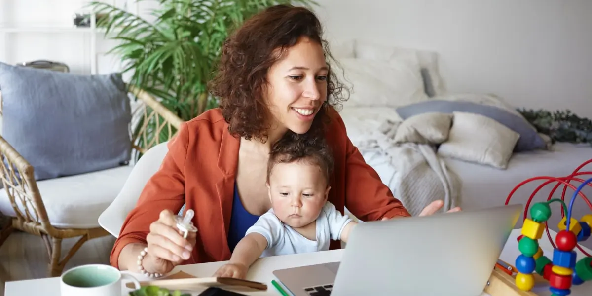 How to write a marketing resume A job applicant sitting at a desk with a baby on their lap, writing their marketing resume on a laptop