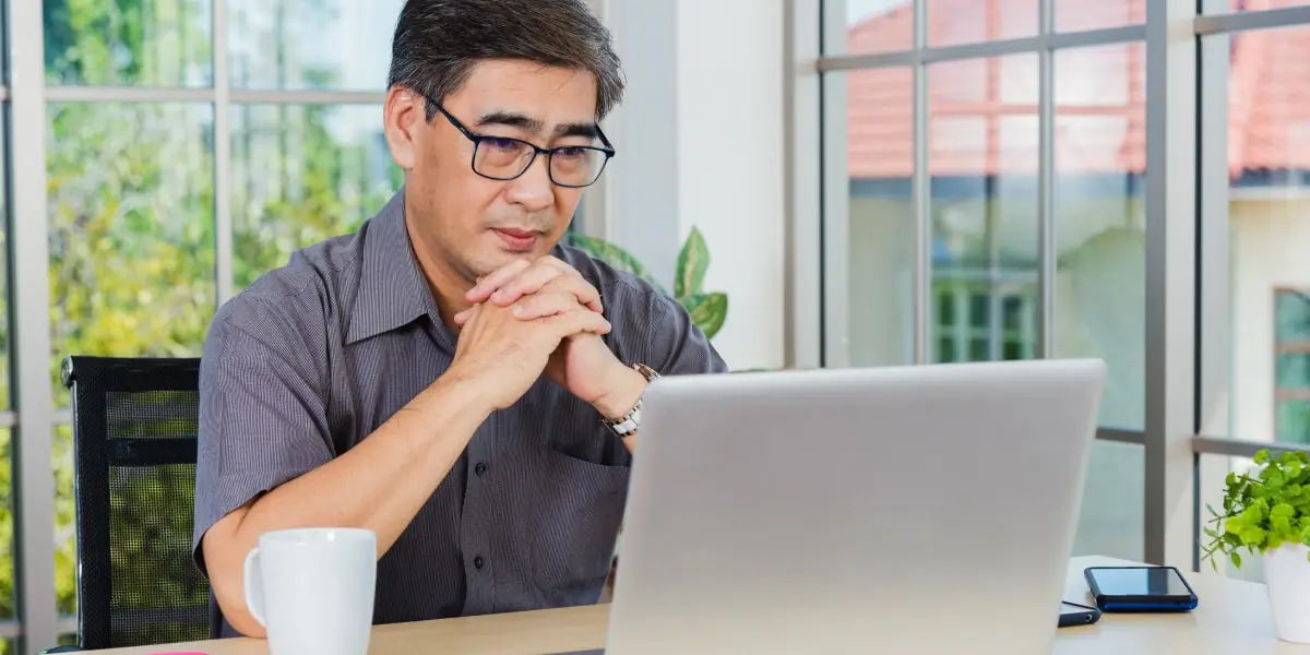 A digital marketing bootcamp student looking at a laptop screen with their hands clasped across their chin
