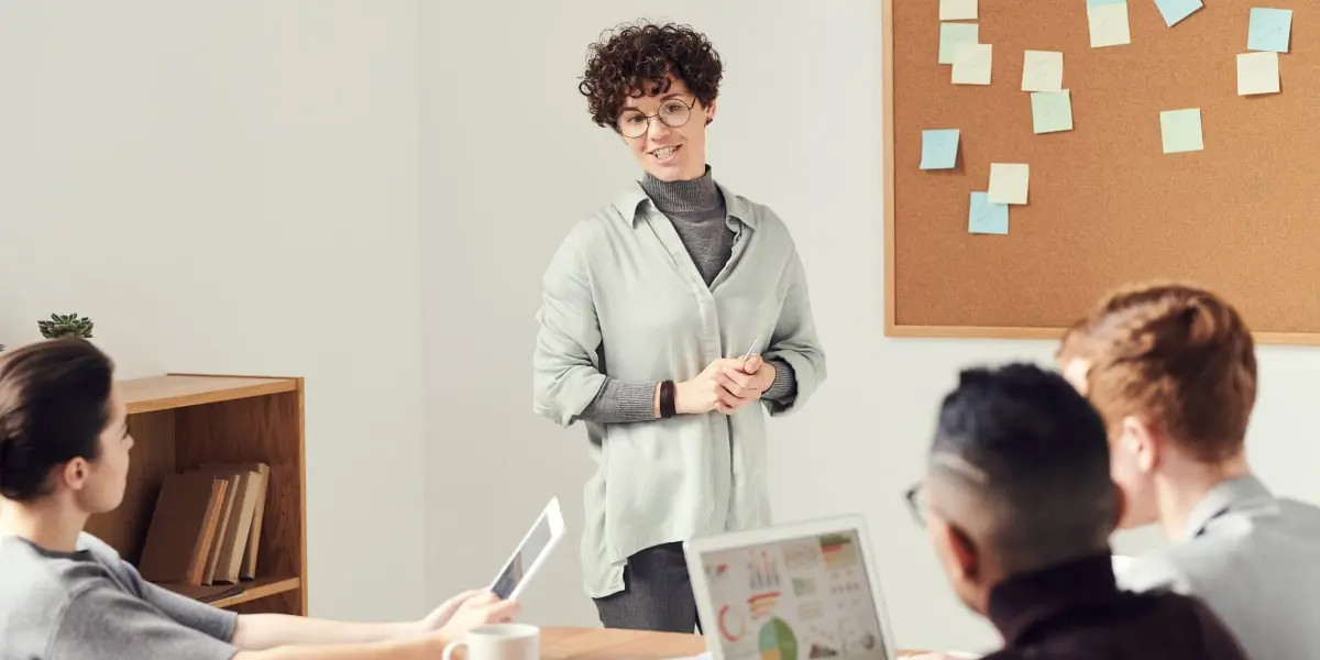A person standing in front of a group of professionals with laptops, giving a presentation