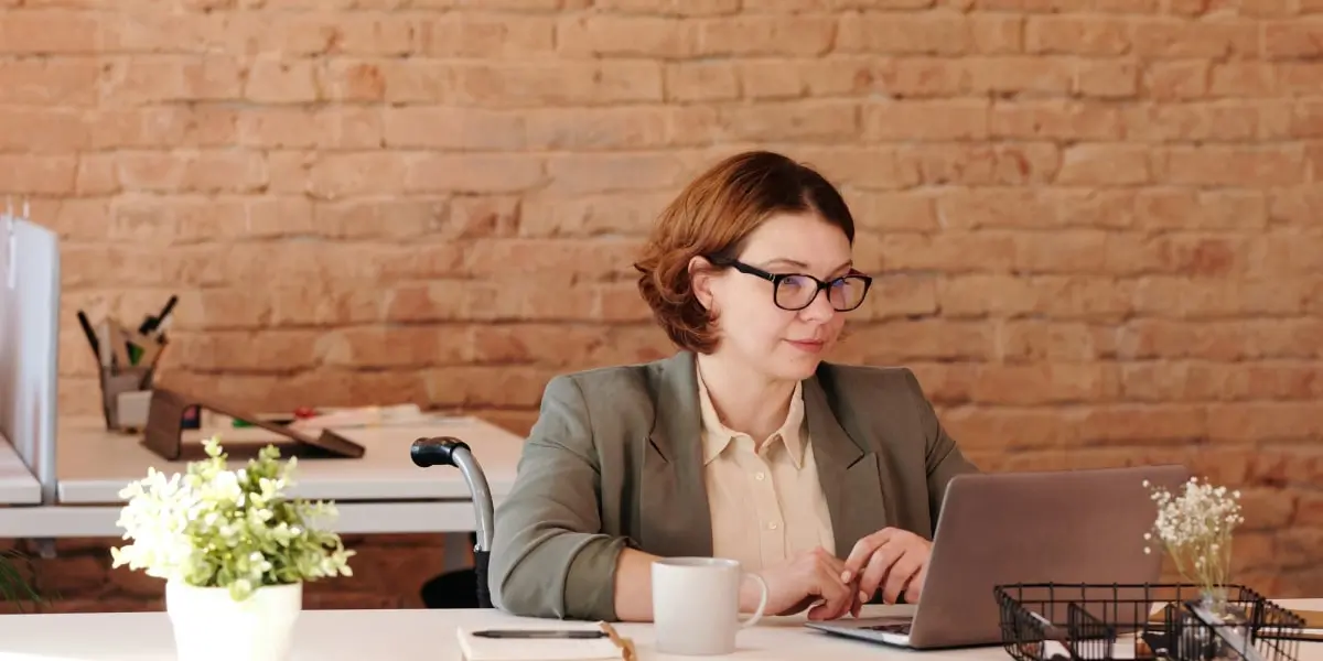 A person sitting in a wheelchair at a cafe table, working on a laptop