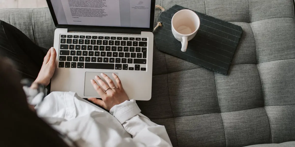A UX writer sitting on a couch with a laptop and cup of coffee
