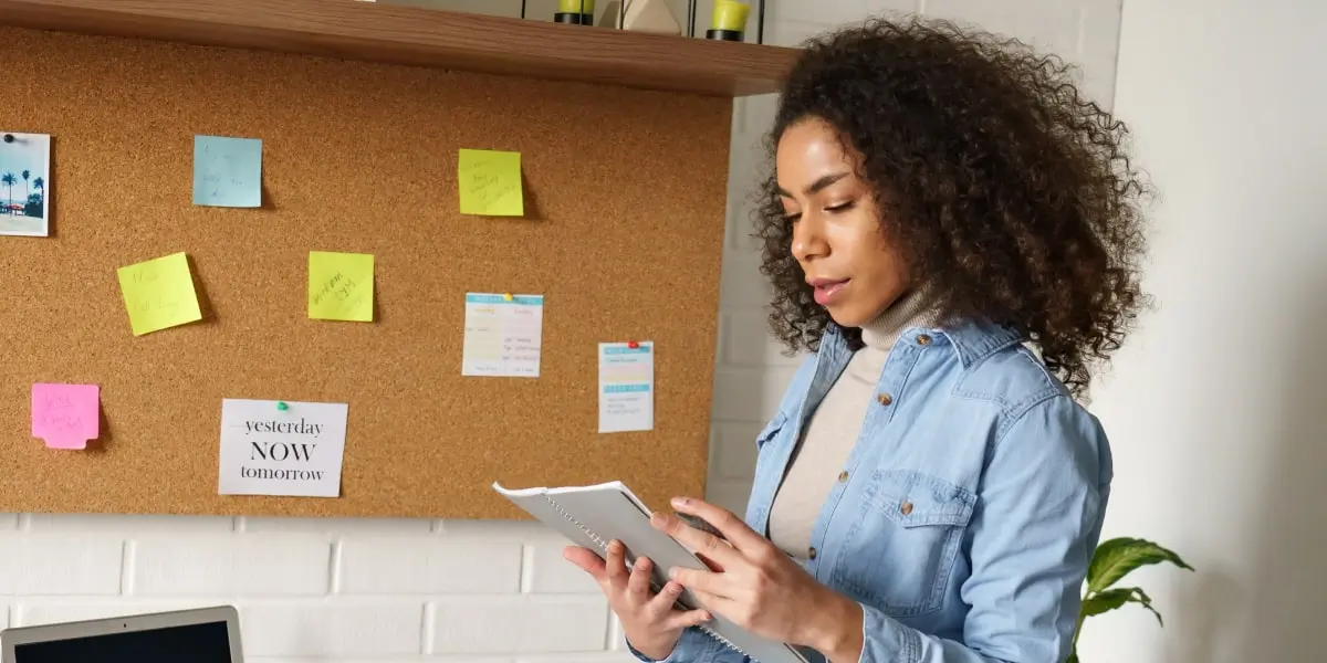 A digital marketing manager looking at a notebook with a wall of Post-It notes in the background