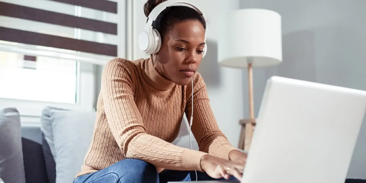 A digital marketing specialist working from home, wearing headphones, leaning forward typing on a laptop