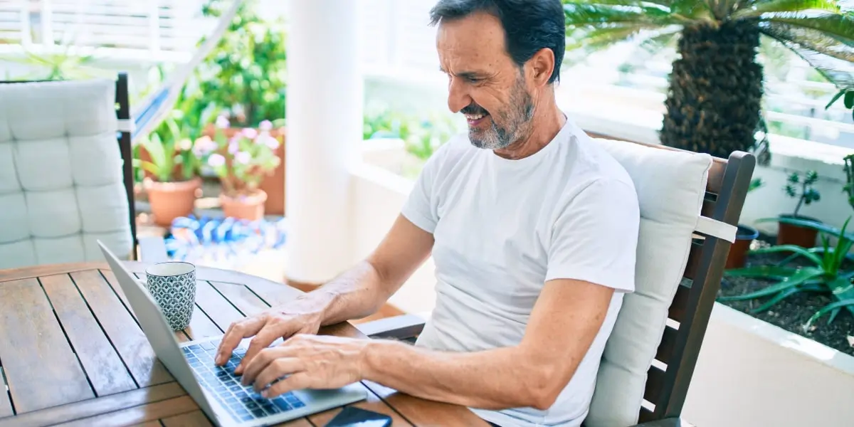A digital marketing manager sitting outside, typing on a laptop, smiling