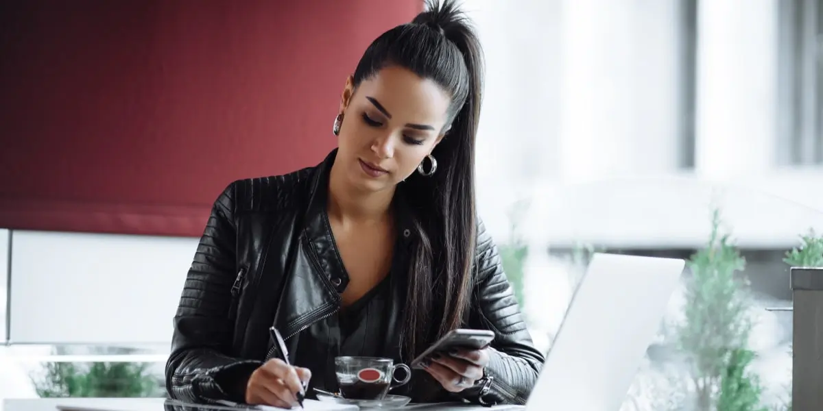 Social media manager interview An aspiring social media manager sitting at a desk, looking at a phone and writing something down
