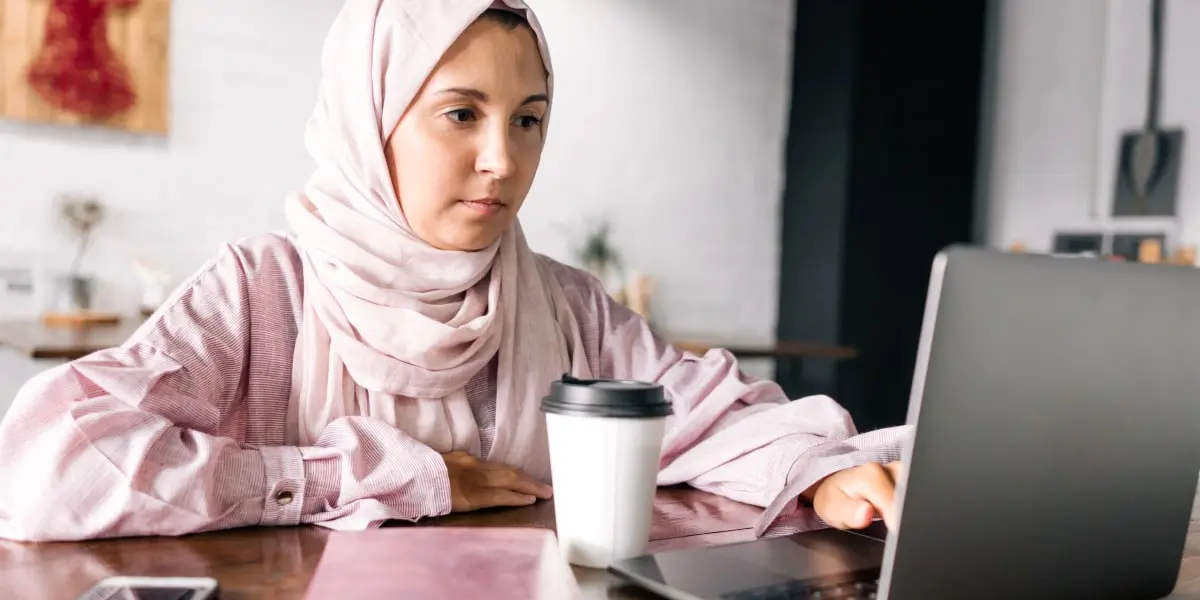 An aspiring tech professional working from home, typing on a laptop with a coffee cup in view