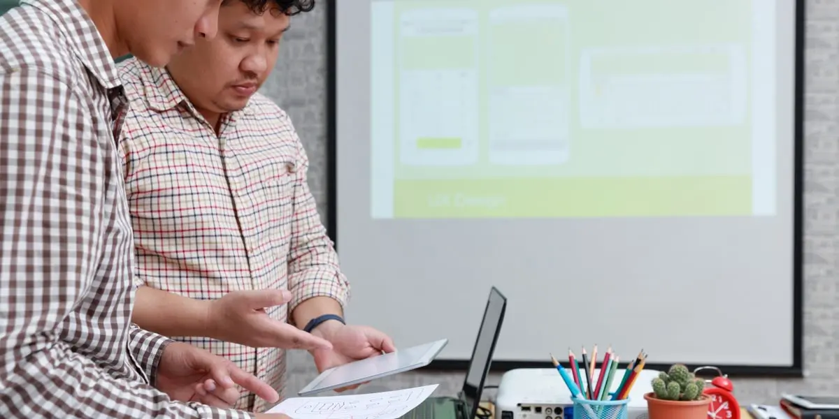 Two UX designers standing in an office, looking at a laptop, working on creating a problem statement for a design project