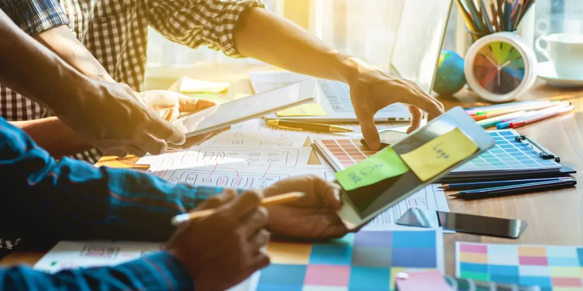 Two designers creating a UX strategy at a table covered in sticky notes and paper prototypes