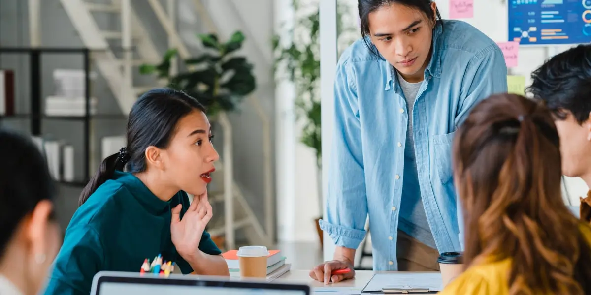 A product manager sitting at a team meeting in a startup office with their colleagues.