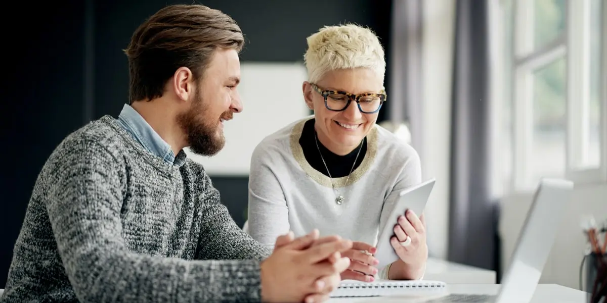 Image of a product manager and project manager sitting in an office discussing something at a laptop.