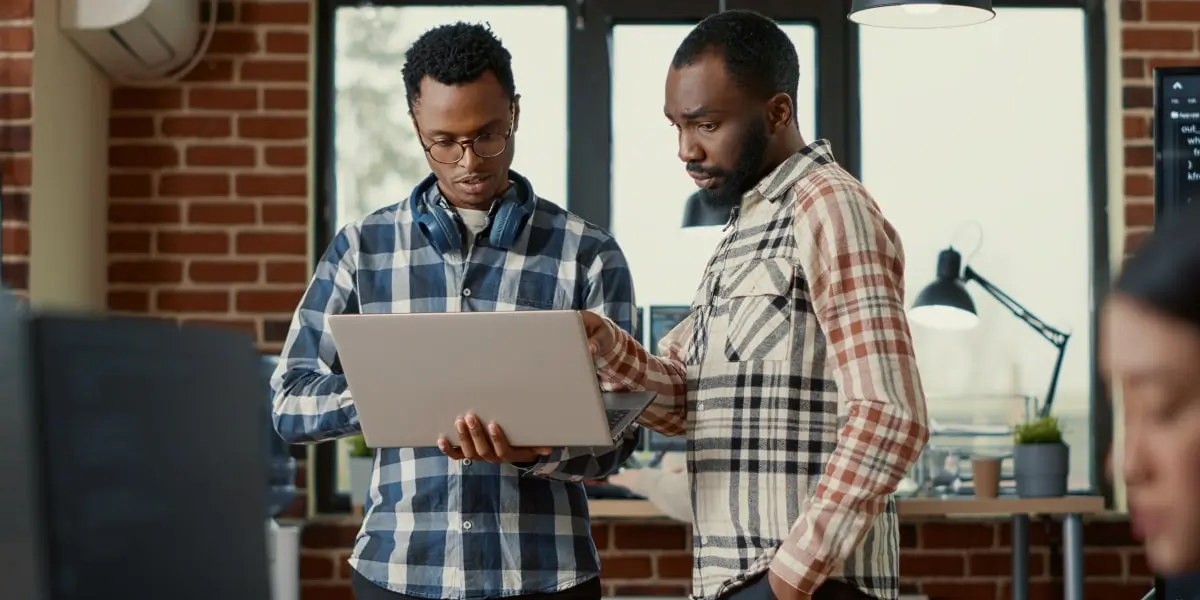 Two cloud computing developers stand in an office looking at a laptop.