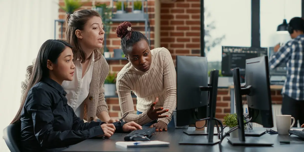 Three developers work at a computer discussing an AWS VPC.