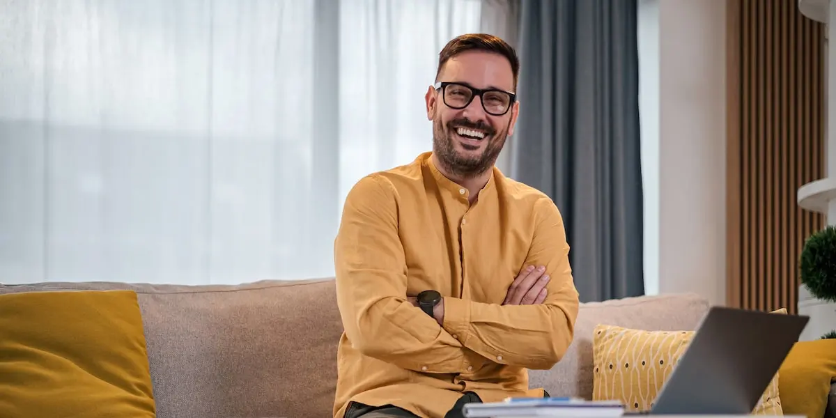 A man sits beside his laptop smiling after earning a product management certification online.