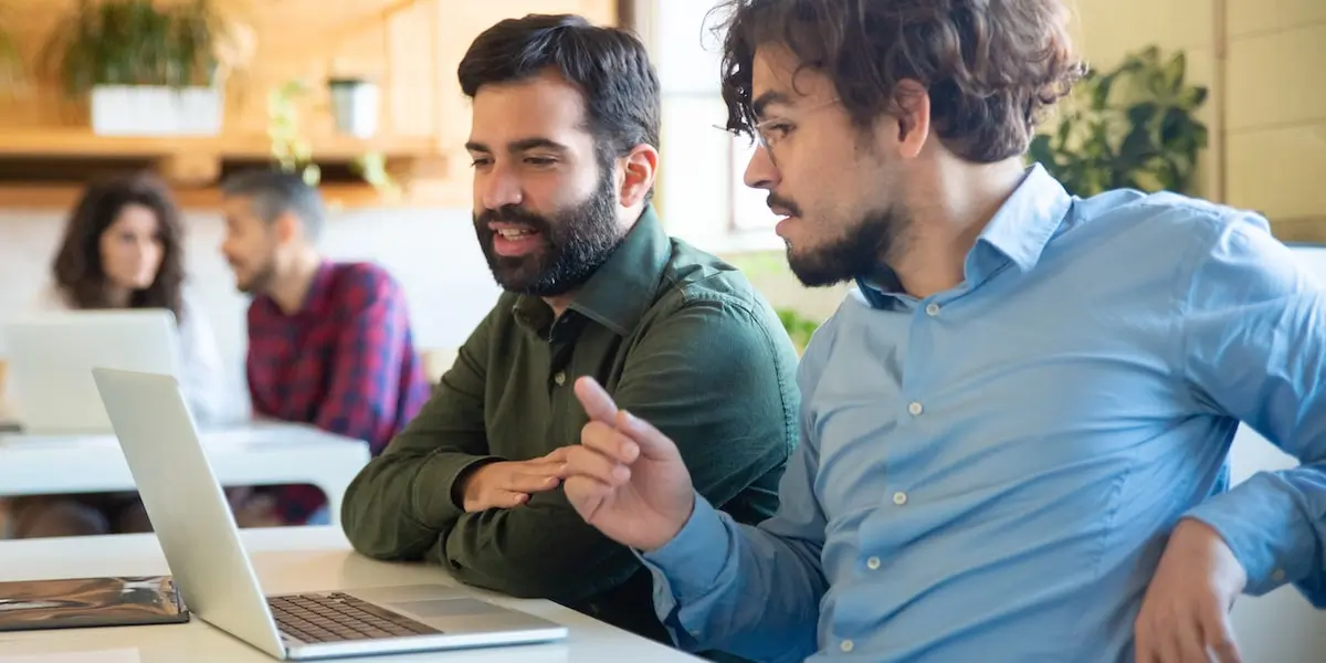 Two cloud engineers sit in an office with a laptop discussing AWS VPCs.