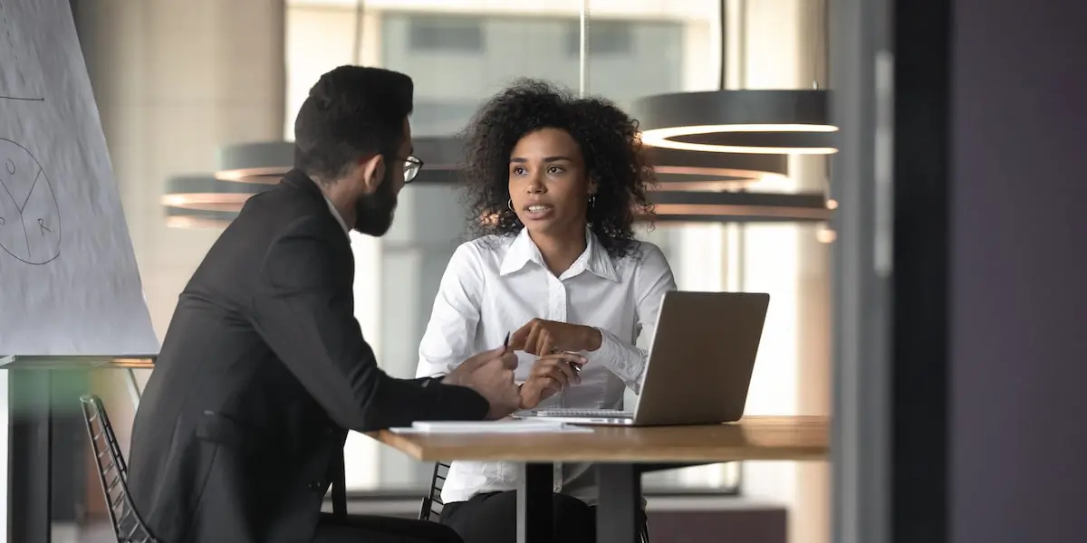 A UX designer and an interviewee sit in an office with a laptop doing a user interview.