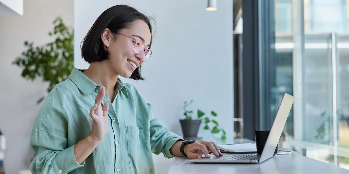 A UX designer conducting user interviews online waves at her laptop.
