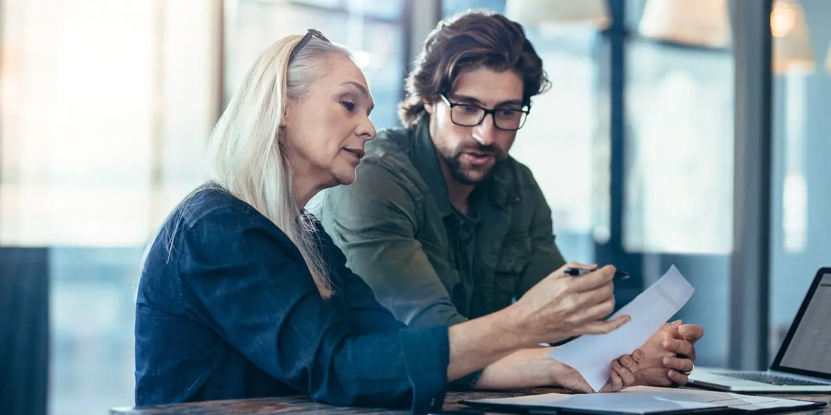 A cloud engineer discusses AWS IAM with their colleague at an office desk.