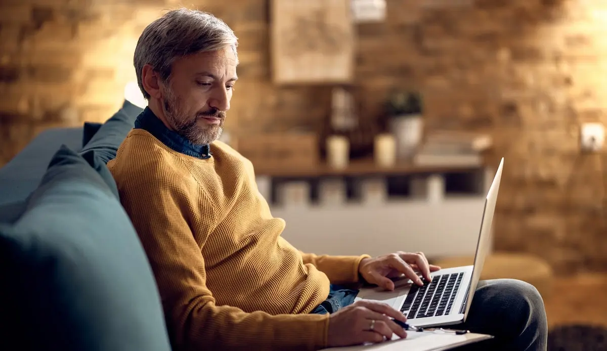 A man sits on his laptop at home working on his product management portfolio.