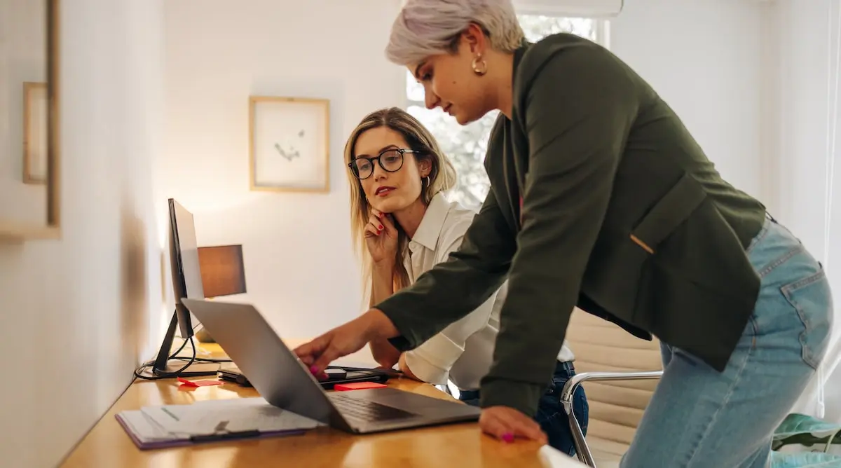 One software engineer shows her colleague how to do something on a computer in a bright office.