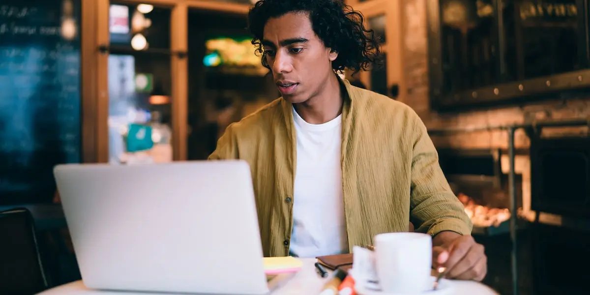 A man sits in a cafe at a laptop learning how to become a coder.
