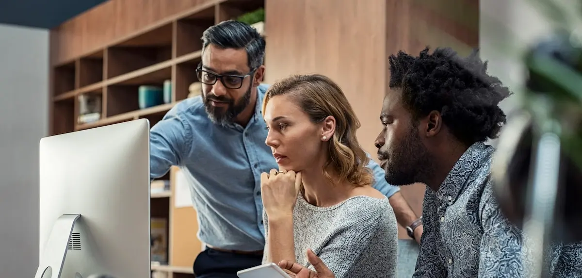 A JavaScript bootcamp graduate points something out to his colleague on a PC in an office.