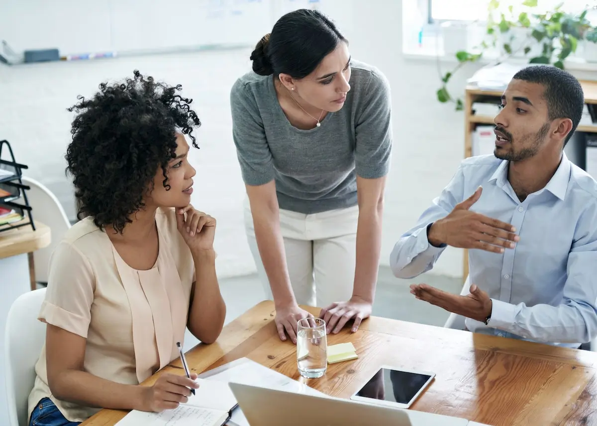 A web developer discusses MongoDB with two of his colleagues in an office.