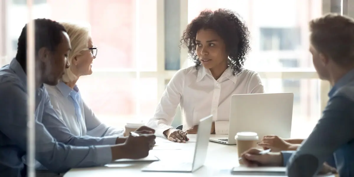 A chief product owner talks to her colleagues in a meeting in a bright office room.