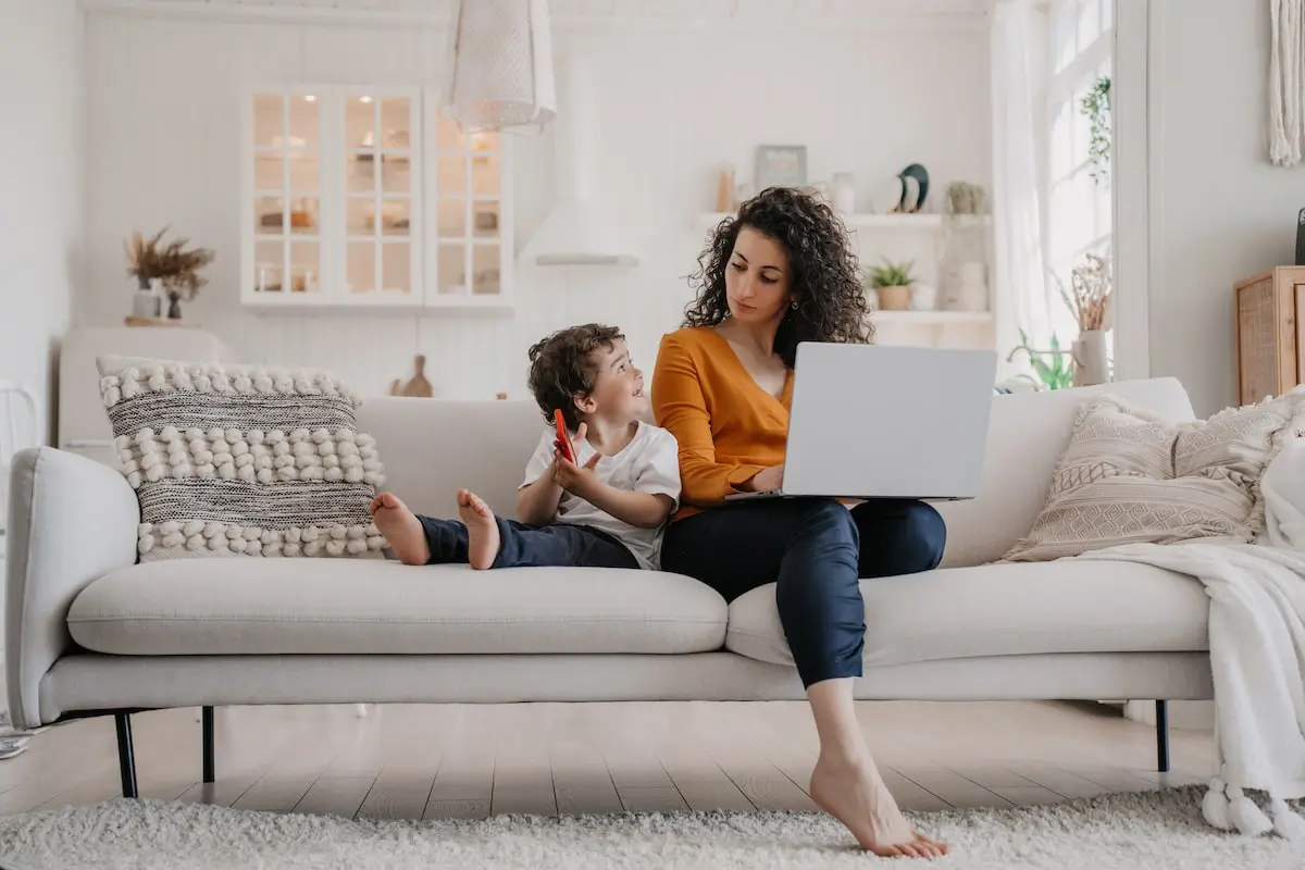 A software engineer works from home sitting on a couch with her son.