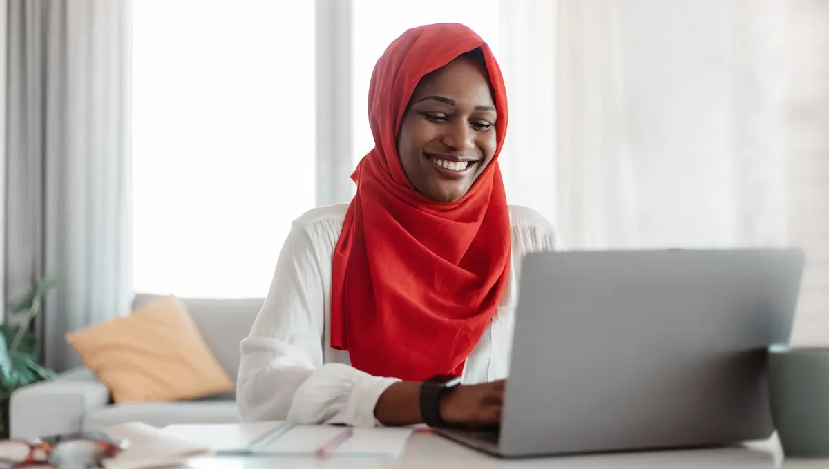 A junior web developer sits at her computer working remotely and smiling.