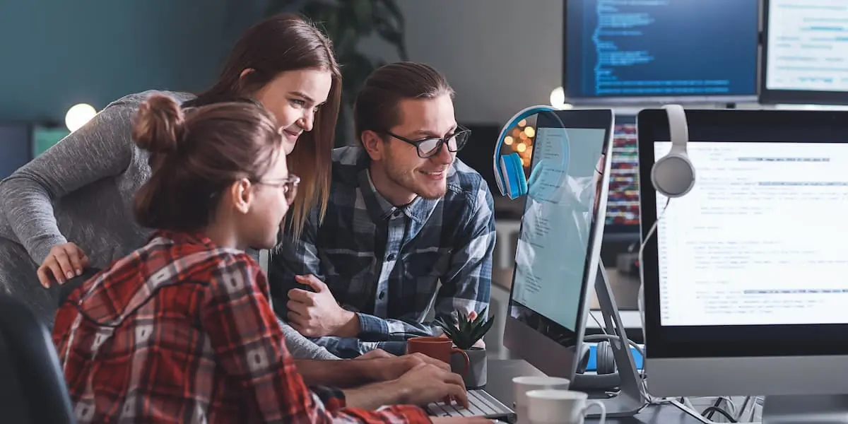 Workers at their entry level IT jobs discuss coding at a computer