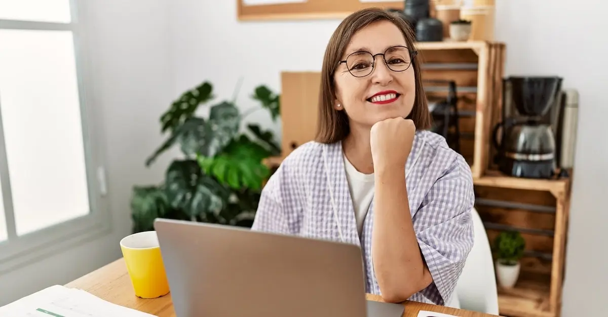 A web developer works from her home office smiling at the camera over her laptop.