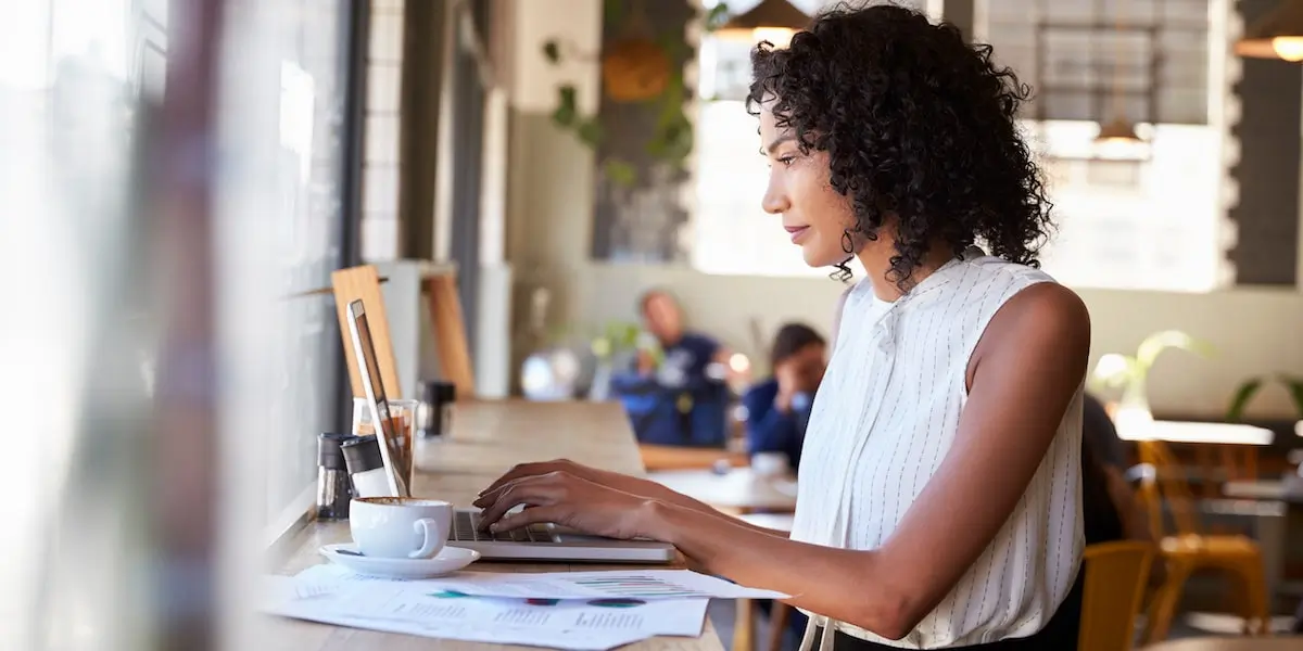 A woman taking a product management program works in a cafe on her laptop.