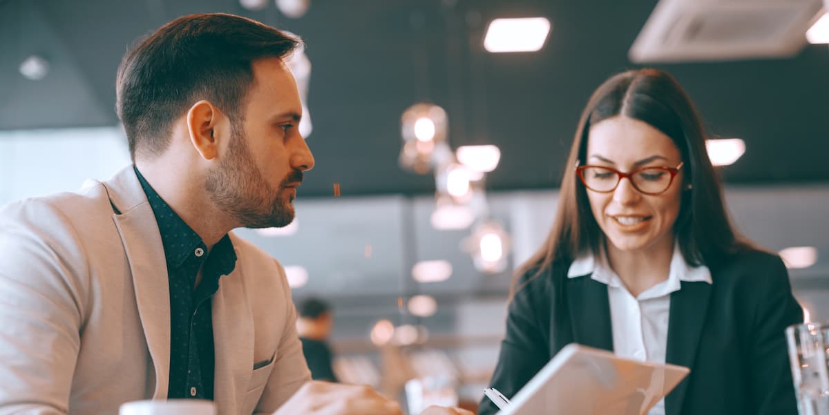 cc at 40 body two 40 year old workers talk at a table with a laptop