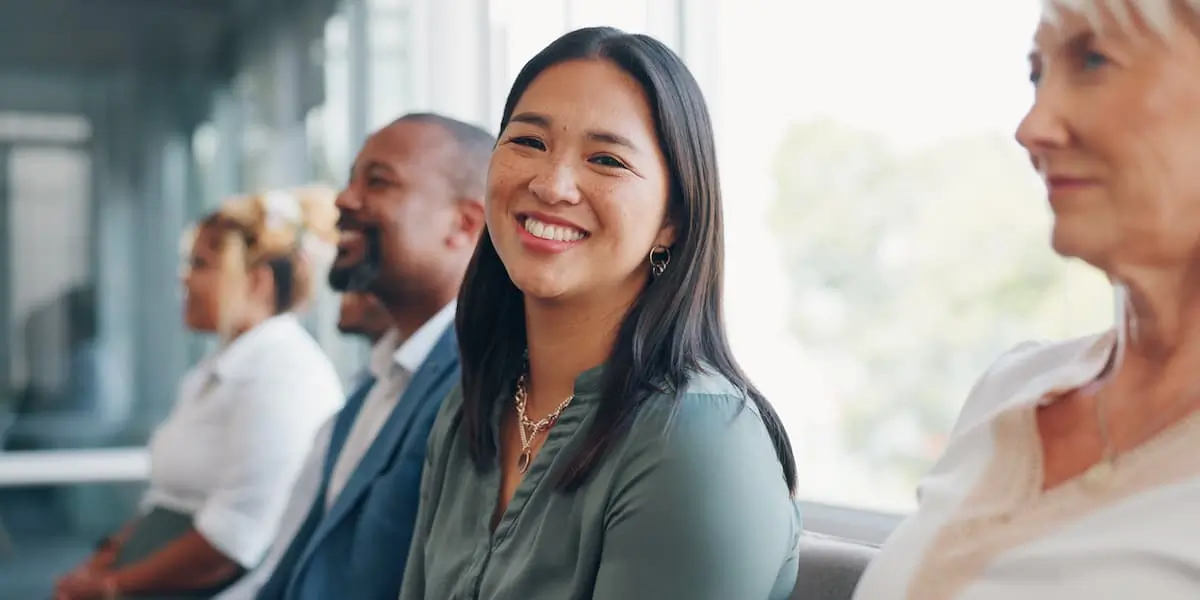 Applicants for a ux design job in a row of chairs with one looking at the camera smiling