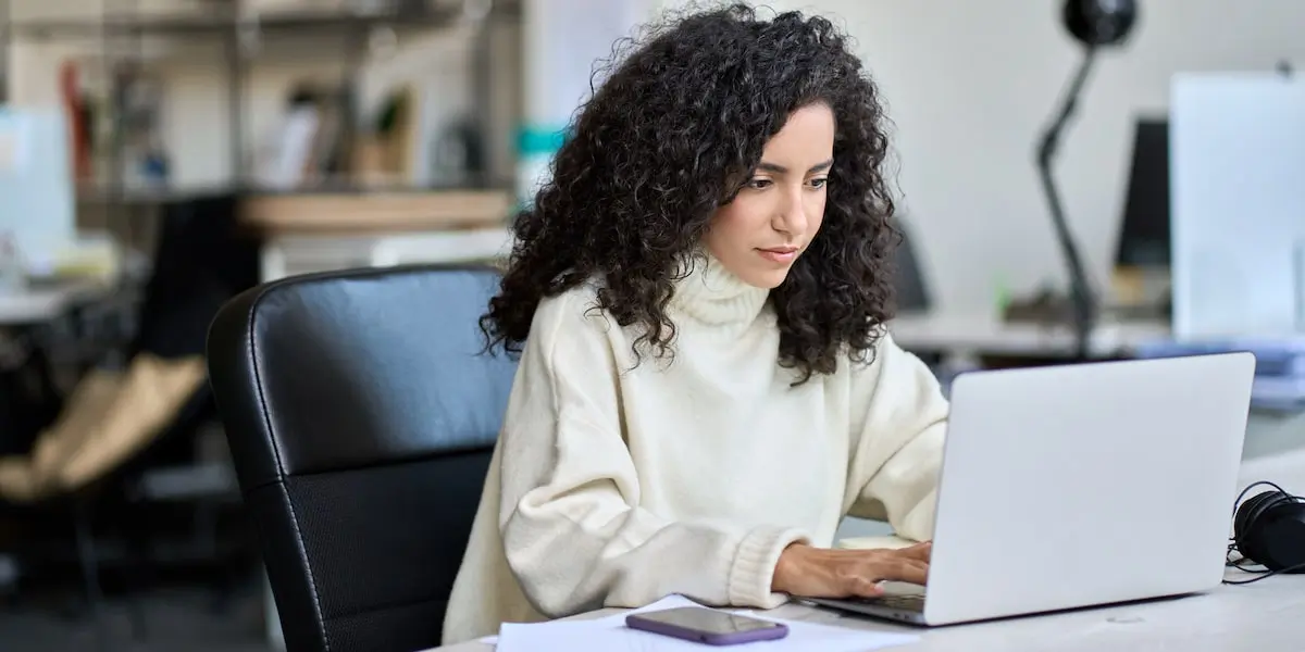 A business intelligence consultant sits in a bright office working at her laptop.
