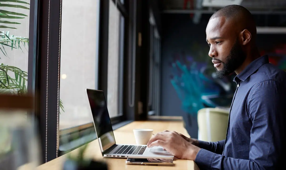 A remote product manager types on his computer with a coffee cup beside him.