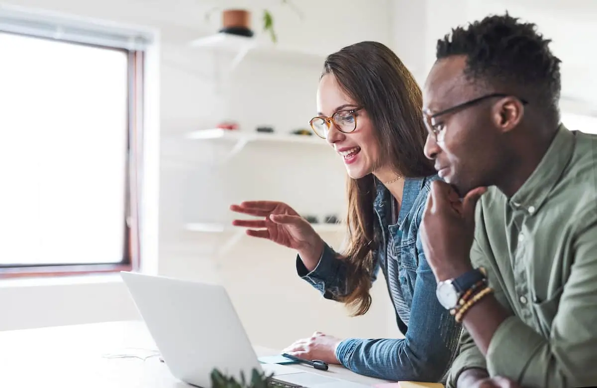 A product operations manager and her colleague have a videocall on a laptop in a bright office.