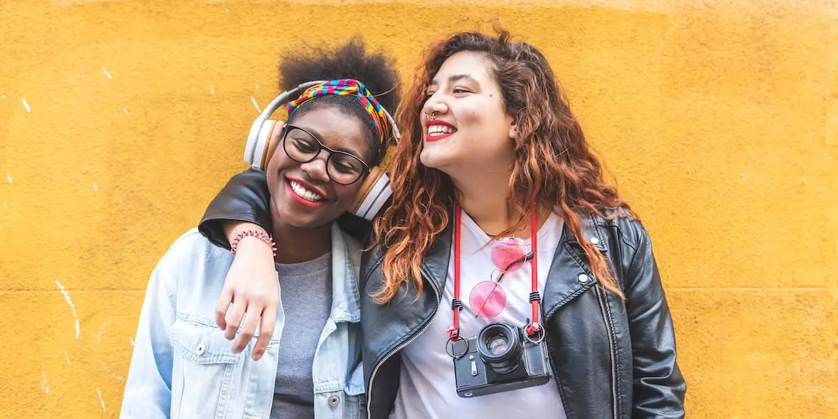 Two students from different graphic design schools smiling together against a yellow wall