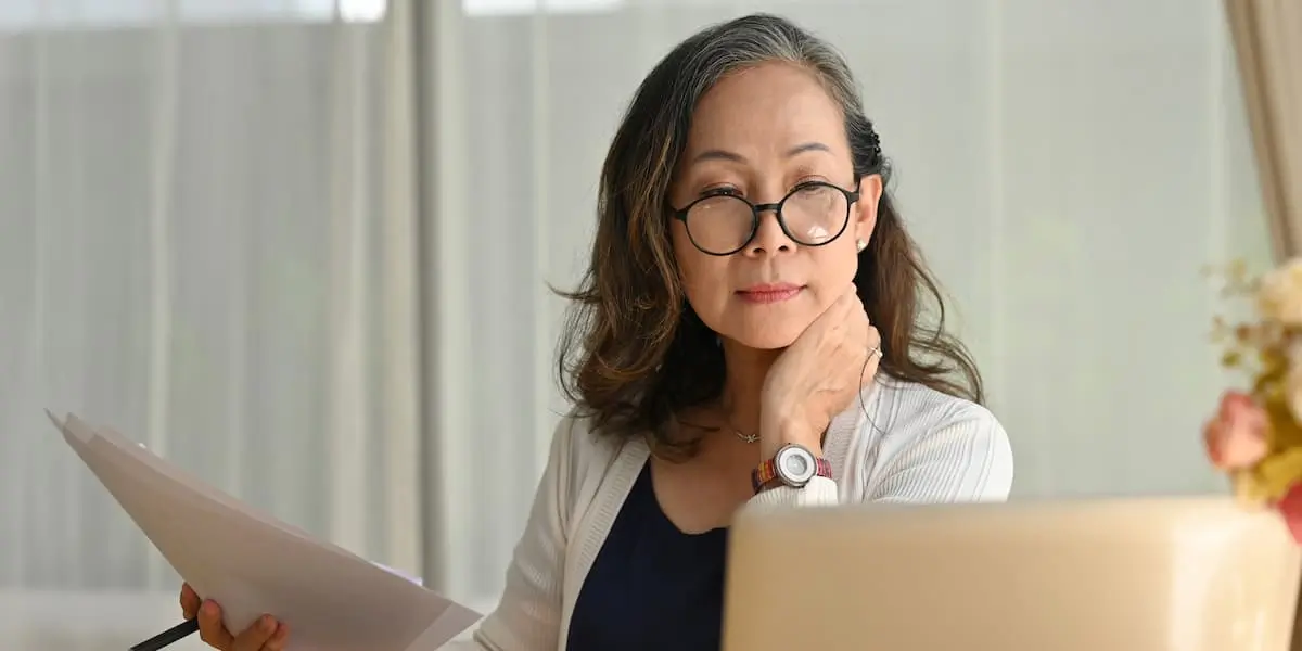 A UX designer sitting at her laptop holding a piece of paper using lateral thinking to problem-solve