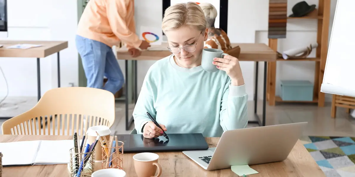A product designer drawing on a pad connected to her laptop in a bright office.