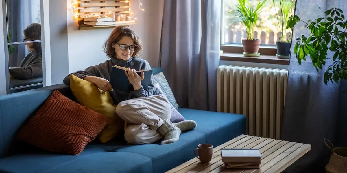 A product designer relaxes on a sofa while reading product design books and drinking a coffee.