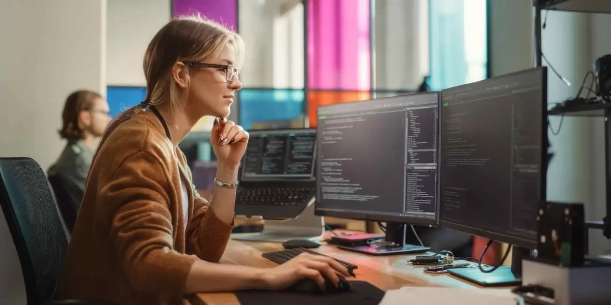 A woman working in tech sits at a computer and codes.