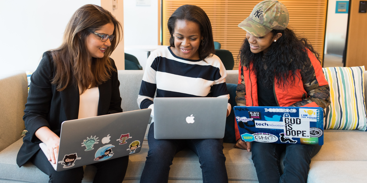Three designers sitting on a sofa with laptops, smiling and chatting