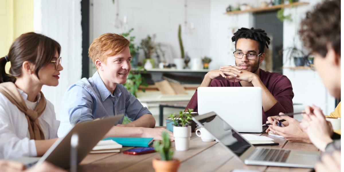 A group of designers from various backgrounds, gathered around a table with their laptops