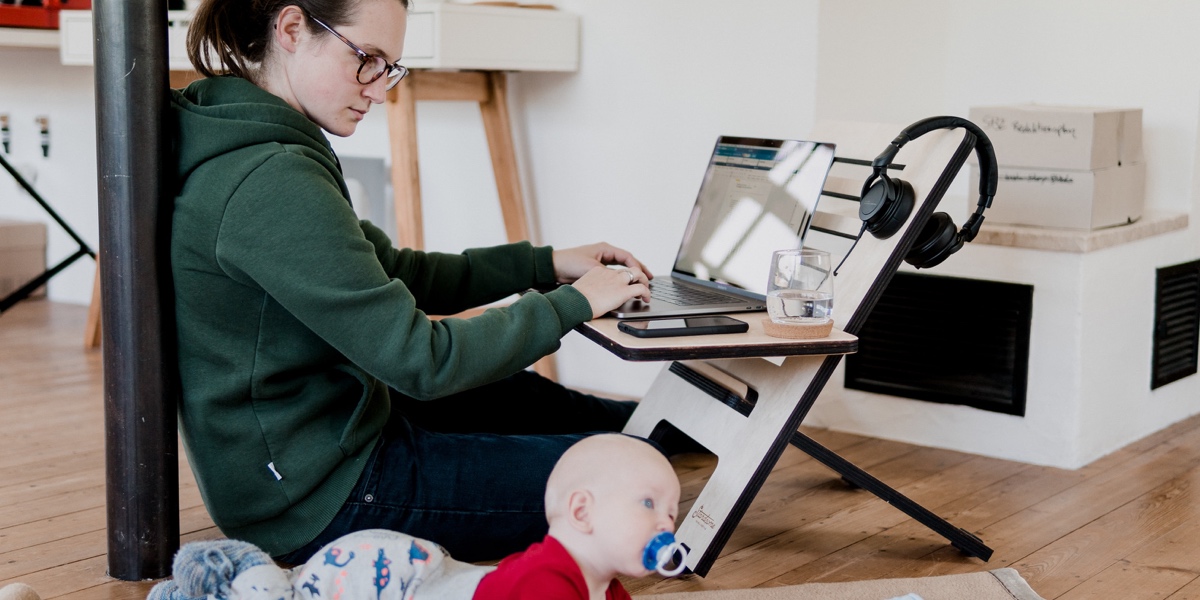 Break into Tech: How to Face Your Career Change Fears A woman sitting at a makeshift desk on the floor, working at a laptop with her infant nearby
