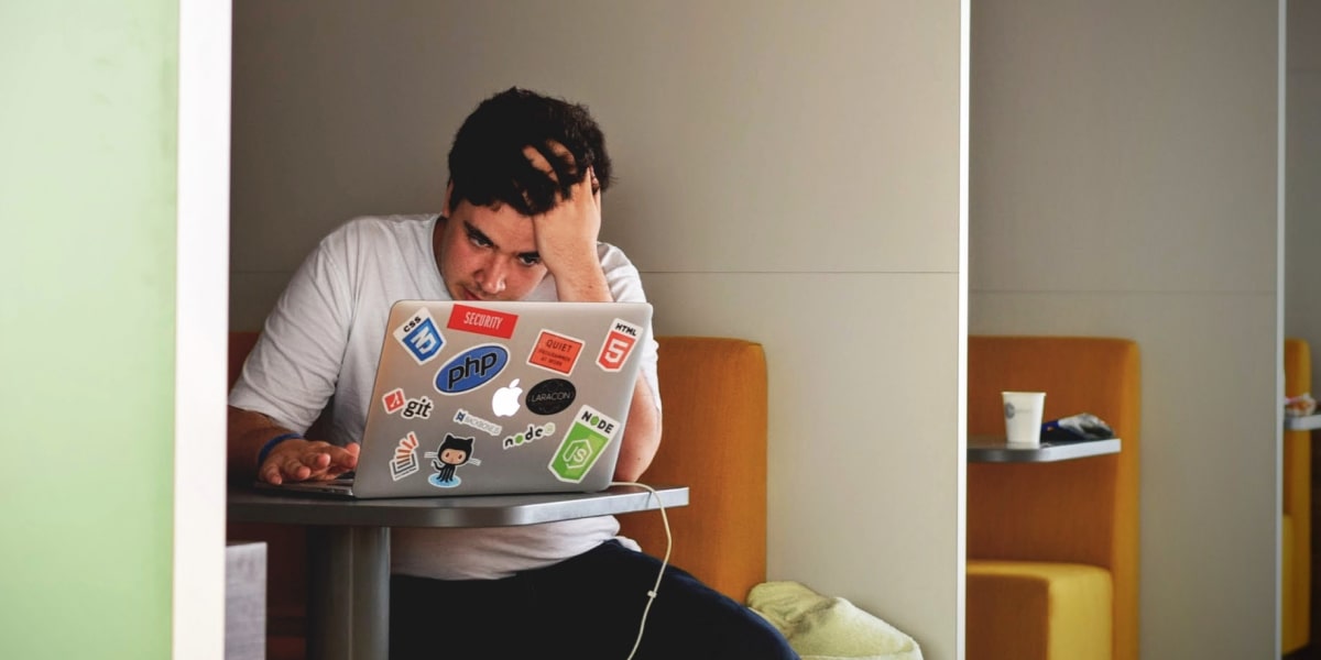 Dark Patters in UX: Why companies use them A man sitting at an office workstation with his hand on his head, staring at his laptop in frustration