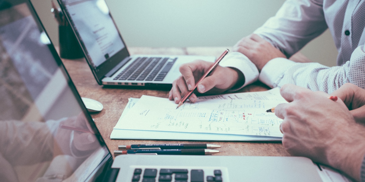 Two designers' hands (close up), working on a set of papers between two laptops