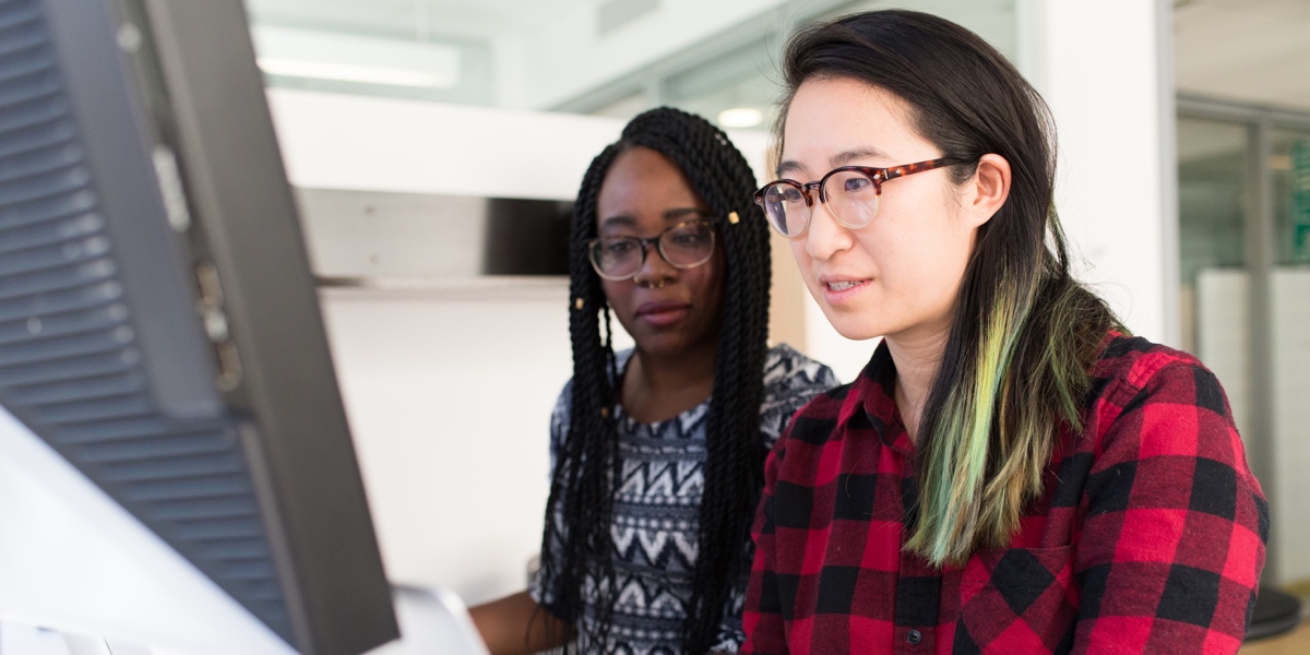 Two women sitting together at a desk, looking at a computer screen
